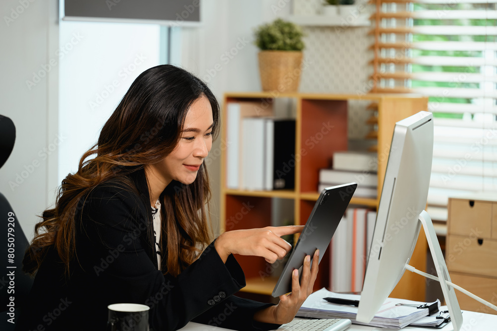 Cheerful young businesswoman sitting at desk and using digital tablet Cheerful young businesswoman sitting at desk and using digital tablet