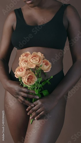 Vertical midsection shot of African American woman in black underwear holding bouquet of roses while posing in studioVertical midsection shot of African American woman in black underwear holding bouqu