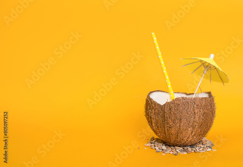 Exotic cocktail served in coco shell, drinking straw and cocktail umbrella on blorange background with space for text. Summer background.