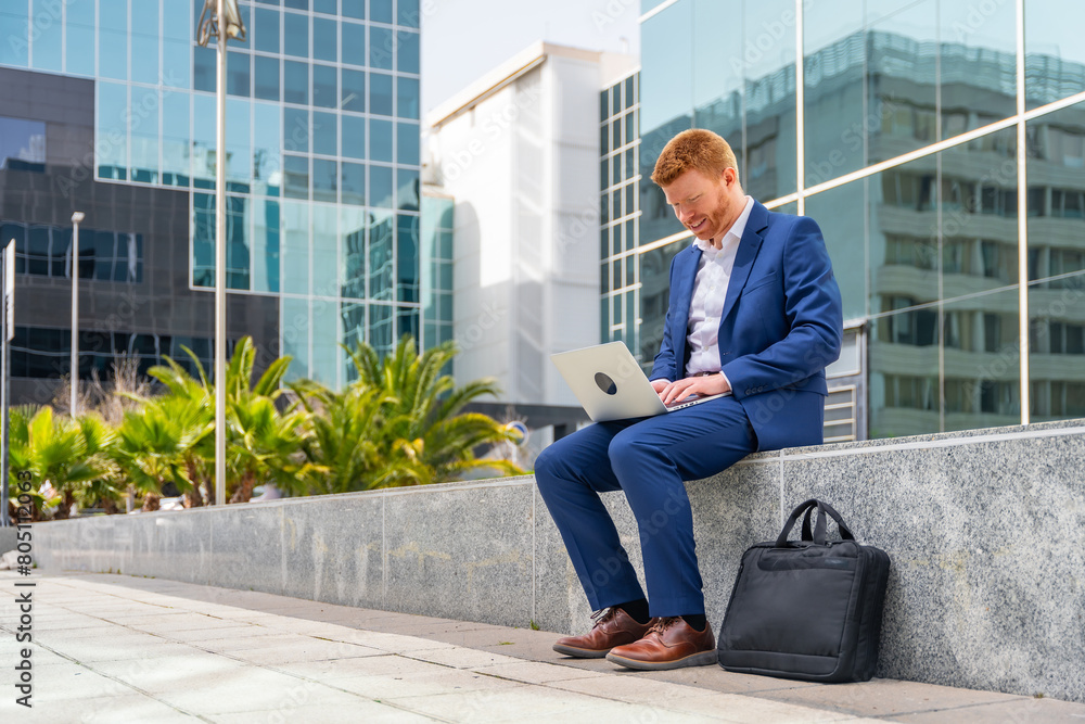 Businessman using laptop sitting outside a financial building Businessman using laptop sitting outside a financial building