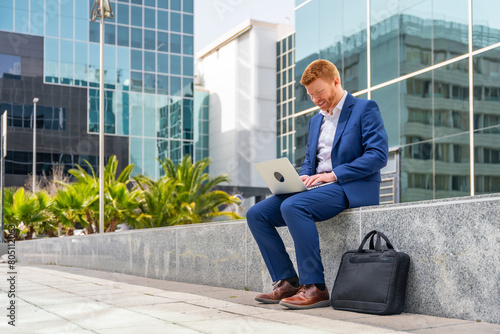 Businessman using laptop sitting outside a financial building © unai
