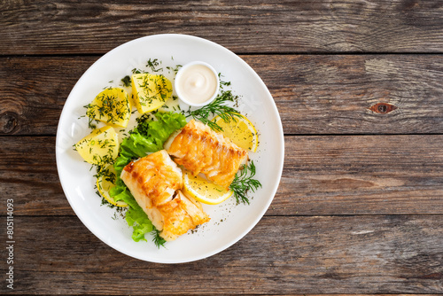 Fried codfish loin boiled potatoes and fresh vegetable salad on wooden table