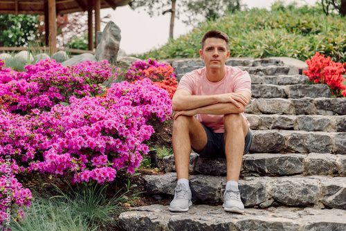 Young caucasian man sit on the stairs in summer flowering park.