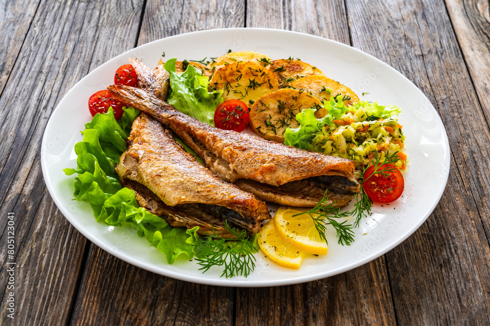 Fried sea bass with fried potatoes and fresh cabbage salad on wooden table
Fried sea bass with fried potatoes and fresh cabbage salad on wooden table
