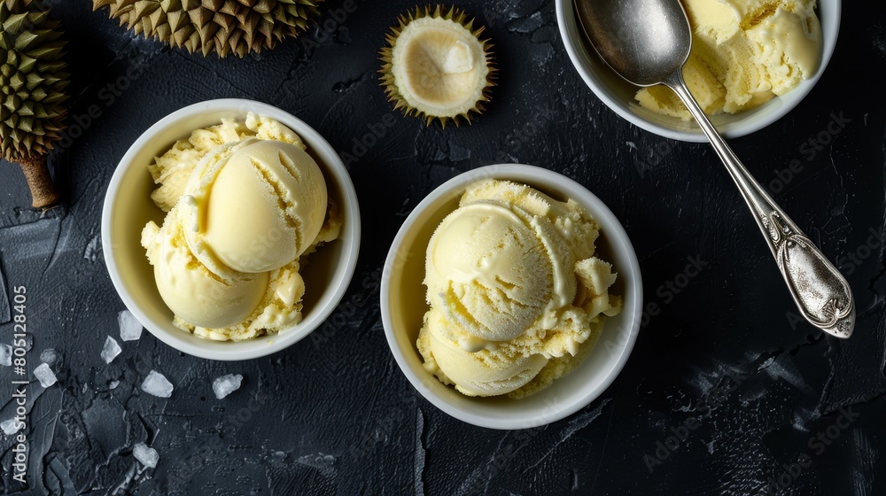 durian ice cream on a black table. A spoon is in one of the bowls. Two durian fruits are also on the table. durian ice cream on a black table. A spoon is in one of the bowls. Two durian fruits are also on the table.