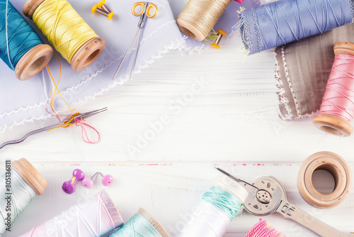  Flat elegant photo of different fabric and sewing tools, sewing accessories, sewing threads, thread spools, needles, pins on the white table with copy space