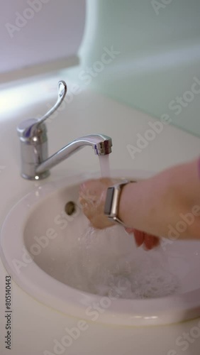 Vertical video. An unrecognizable female doctor in a purple medical suit washes her hands thoroughly in the washbasin before the procedure, standing indoors