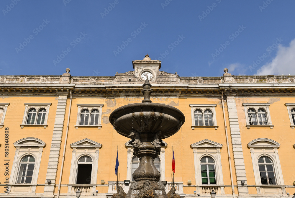 Fototapeta premium Low-angle view of the town hall of the popular holiday resort in the Italian Riviera of Ponente, with the stone fountain in the foreground, Alassio, Savona Liguria, Italy