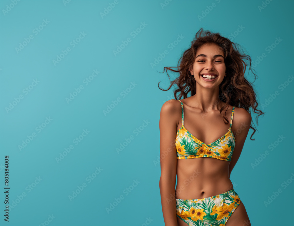 Naklejka premium Portrait of smiling young woman in swimsuit isolated on blue background, summer-themed designs, copy space