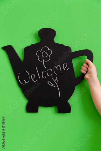 A real blackboard in the form of a teapot with a drawing in the hands of a child on green background
