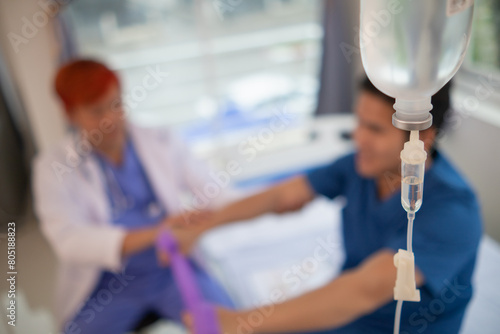 An iron stand to hang saline bottle high to deliver saline via catheter to an intravenous patient lying on patient bed. Medical concept in which doctor gives saline solution to patient through vein photo