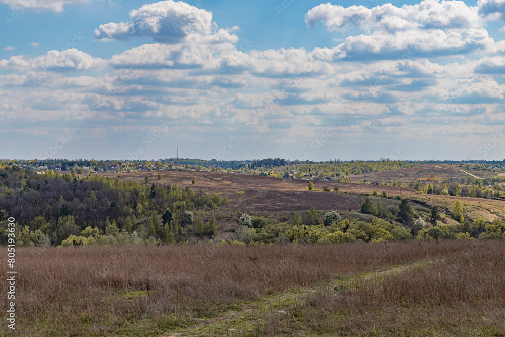 spring landscape, hillsides, blossoming trees, rural houses in the distance and blue sky with white clouds spring landscape, hillsides, blossoming trees, rural houses in the distance and blue sky with white clouds