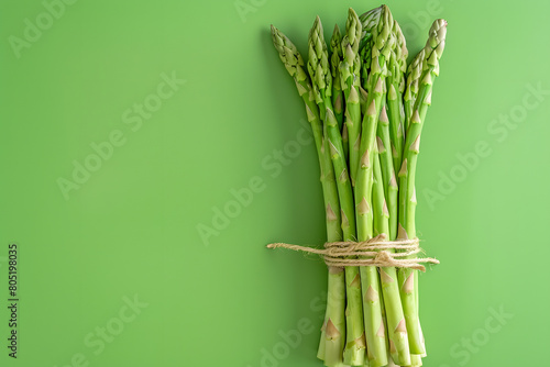 A bundle of fresh asparagus spears  arranged vertically  against a fresh green background with copy space to discuss health benefits or spring recipes