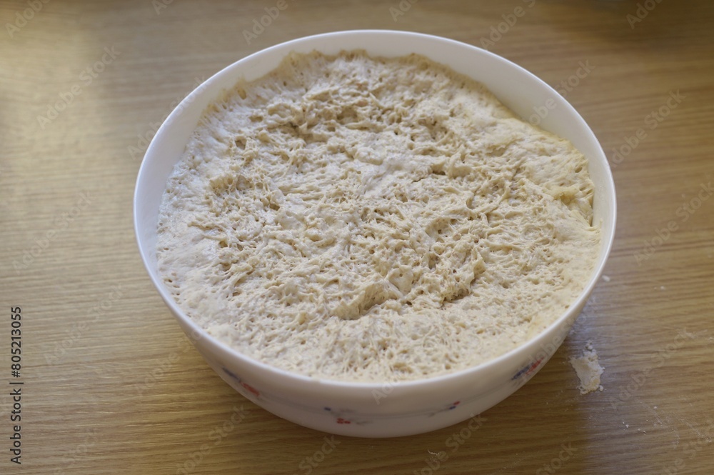 a container with a raw yeast dough on the wooden kitchen table. a container with a raw yeast dough on the wooden kitchen table.