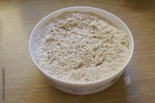 a container with a raw yeast dough on the wooden kitchen table.