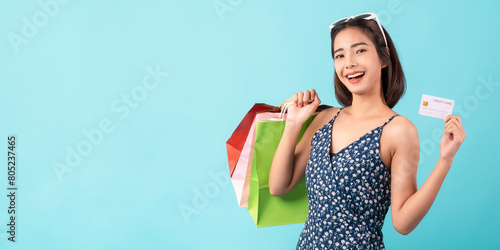 Young Asian woman standing on a blue background and hand holding shopping bags with credit card.