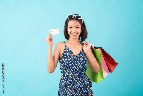 Young Asian woman standing on a blue background and hand holding shopping bags with credit card.