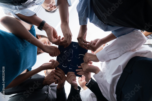 Below view of diverse corporate officer workers collaborate in office connecting puzzle pieces as partnership and teamwork concept. Unity and synergy in business idea by merging jigsaw puzzle. Concord