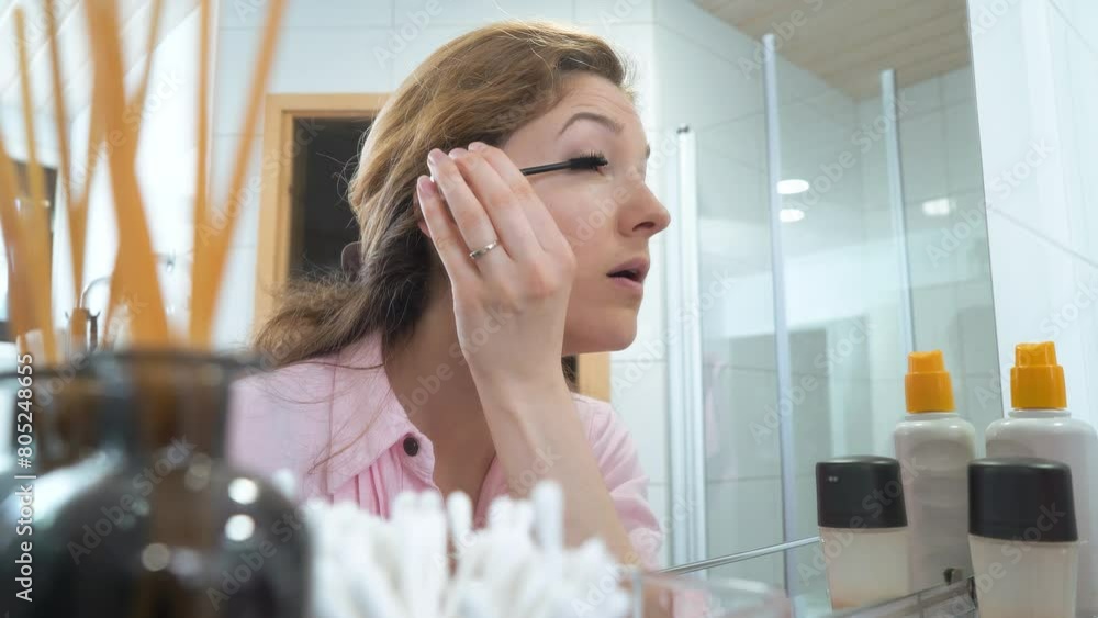 Beautiful caucasian middle aged woman paints her eyelashes with an eyelash brush in the bathroom Beautiful caucasian middle aged woman paints her eyelashes with an eyelash brush in the bathroom