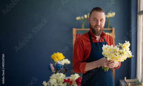 A florist creating a beautiful bouquet of spring daffodil flowers works in his flower shop. Small business owner