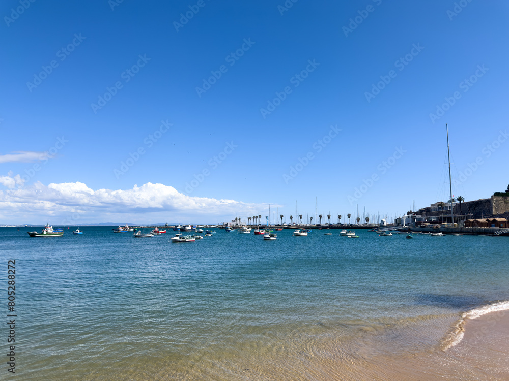 Calm beach with crystal clear water and boats in the background.