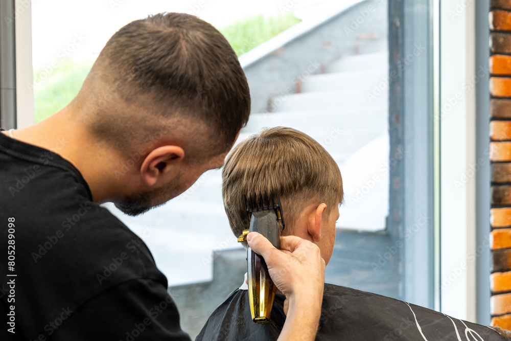 Fototapeta premium A child with very beautiful blond hair is in a barbershop and is being milled with a special hair milling machine.