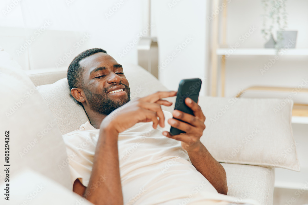Happy African American man sitting on a black sofa, typing a message on his mobile phone He is relaxing at home, enjoying the modern lifestyle and wireless technology The cozy apartment provides a Happy African American man sitting on a black sofa, typing a message on his mobile phone He is relaxing at home, enjoying the modern lifestyle and wireless technology The cozy apartment provides a