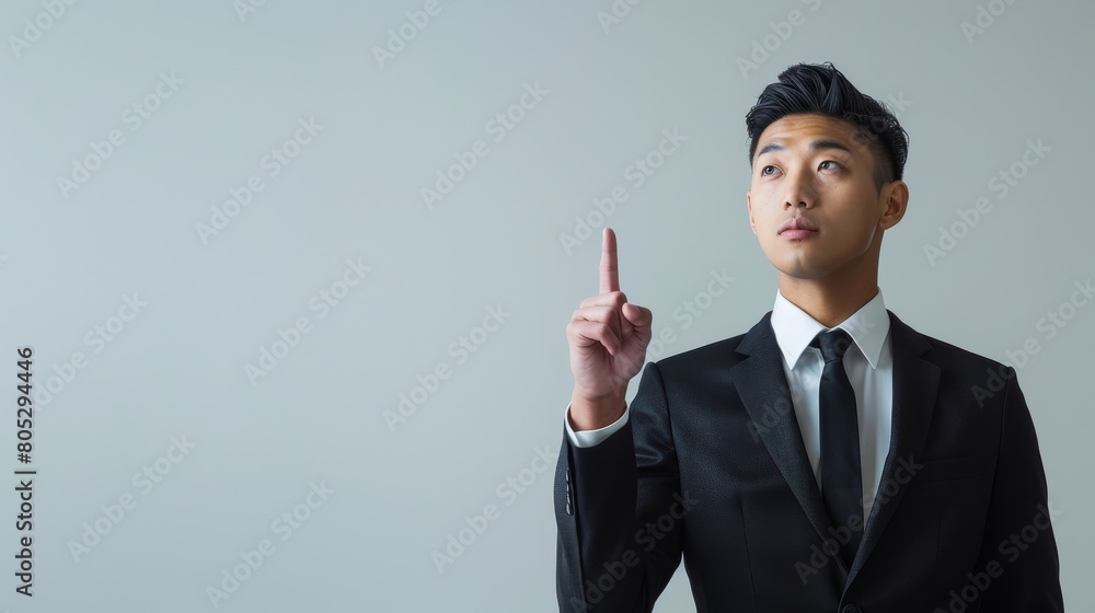 Young Asian Businessman Pointing Upwards Thoughtfully Young Asian Businessman Pointing Upwards Thoughtfully