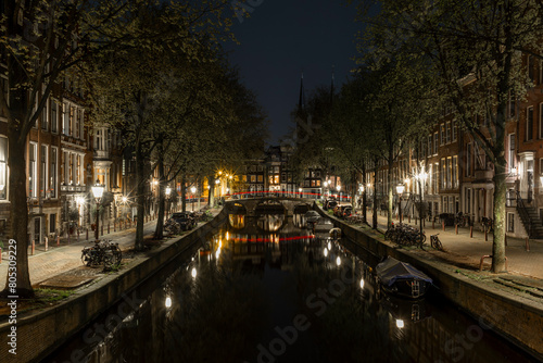 Houses and bridges reflecting on the calm waters of the canals in Amsterdam at night with cars light trails