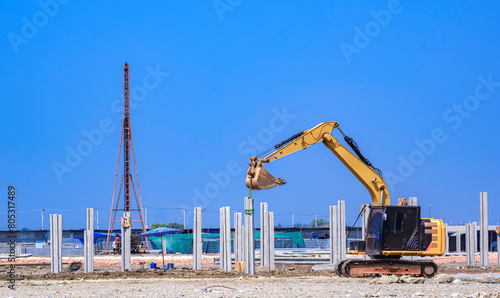 Excavator with pile driver machine are working to installing many precast concrete piles for industrial building foundation structure on the ground in factory construction site area