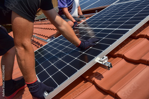 Dachdecker beim Aufbau einer Photovoltaikanlage auf einem neu gedeckten Ziegeldach: Die Endklemmen für die der Solarmodule sind am Ende der Schienen befestigt