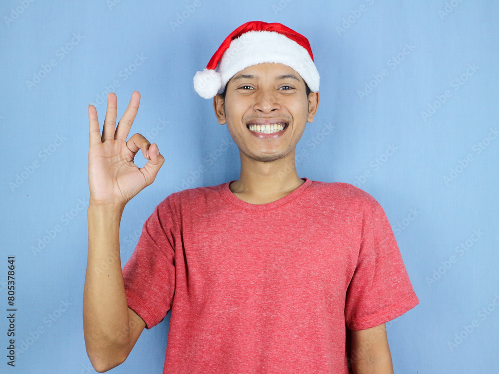 Handsome asian man in red christmas cap with ok gesture looking at camera. Christmas sale concept. Handsome asian man in red christmas cap with ok gesture looking at camera. Christmas sale concept.