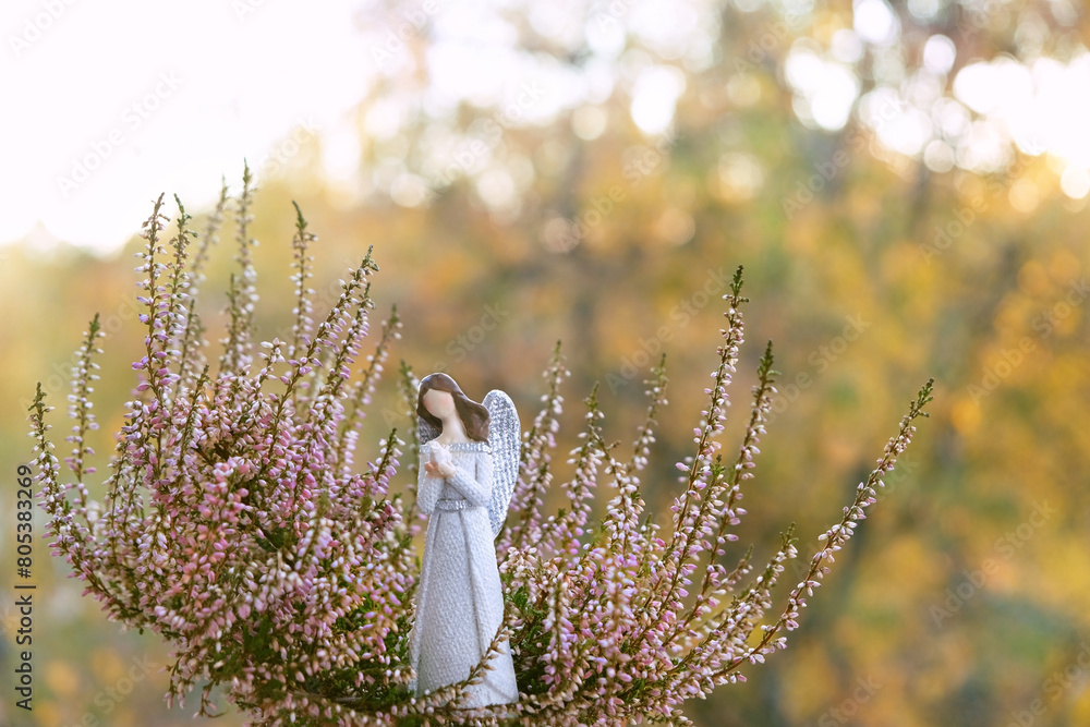 Naklejka premium angel figurine and heather flowers close up in garden, sunny abstract natural background. Beautiful scene. Religious church holiday. symbol of faith in God, pray, believe, christianity.