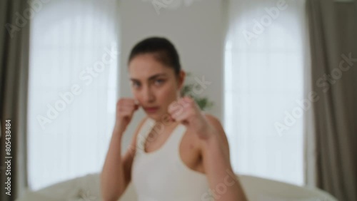 Slim and athletic girl in sportswear doing taekwondo exercises at home in living room. Young woman is practicing punches and kicks, doing martial arts. She is focused and determined
