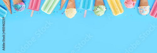 Selection of colorful pastel ice cream cones and popsicle summer frozen desserts. Above view top border on a blue banner background. Copy space.