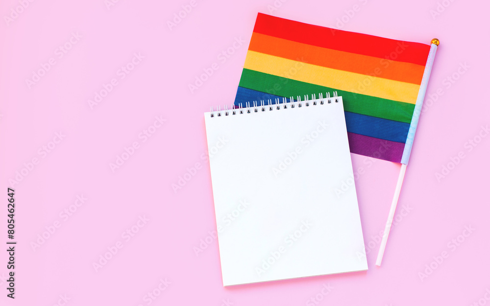 Blank mock up notebook on rainbow LGBTQ flag, pink background. June proud pride month parade, gay marriage, coming out day concept, human rights, tolerance. Flat lay, top view place for text or logo Blank mock up notebook on rainbow LGBTQ flag, pink background. June proud pride month parade, gay marriage, coming out day concept, human rights, tolerance. Flat lay, top view place for text or logo