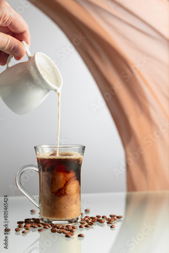 A man's hand pours cream into a glass of coffee.