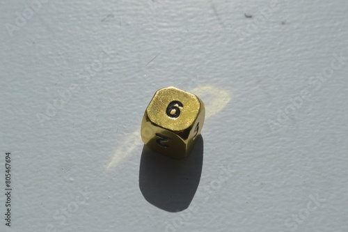 Gold D6 die showing 6 in sunlight on white background