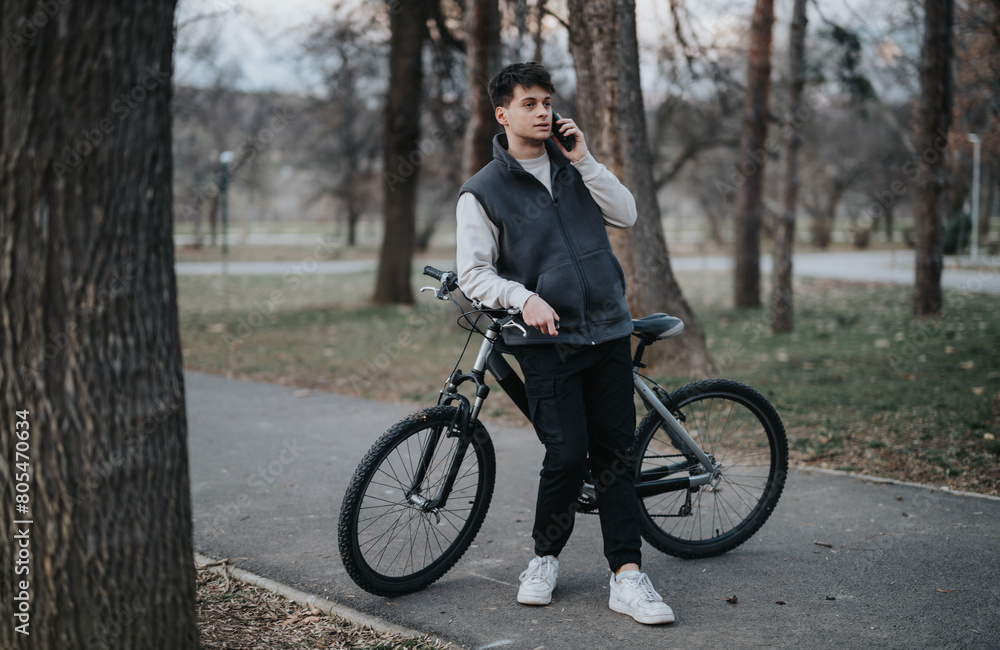 Obraz premium Teenager enjoying a peaceful outdoor setting while on a phone call, leaning on a bicycle in a park.