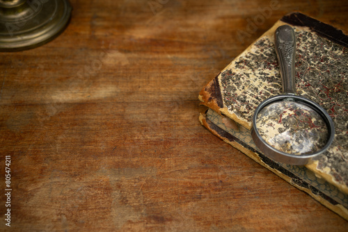 A vintage antique book with a magnifying glass is lying on a wooden table. A photo of the old background for the text.