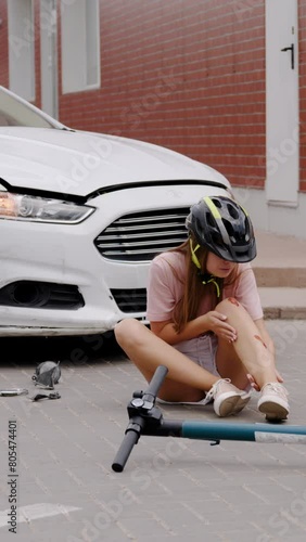 Car and electric scooter collision reveals woman driver injured clutching leg in pain vertical video. Car and electric scooter accident woman driver grimaces in agony holding her injured leg.