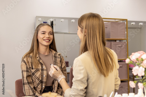 Process of makeup or eyebrow coloring in the salon. Communication between master and client. Soft focus. Smiling young woman