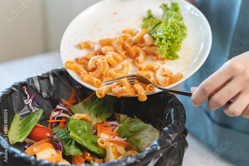 Compost from leftover food in the meal in household, female hand holding left over meal use fork scraping waste, rotten vegetable throwing away into garbage, trash or bin. Environmentally responsible photo
