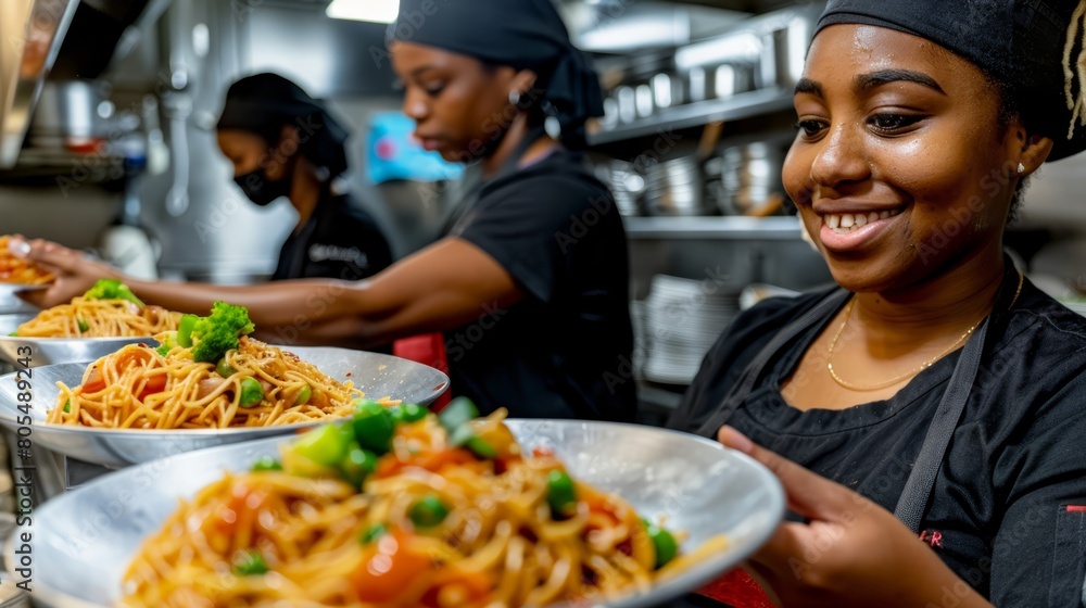   A woman stands in a kitchen, holding a plate heaped with noodles Broccoli florets rest beside the dish