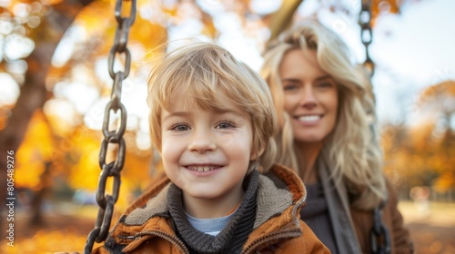  A woman sits next to a young boy on a swing in a fall park Leaves scatter the ground beneath them