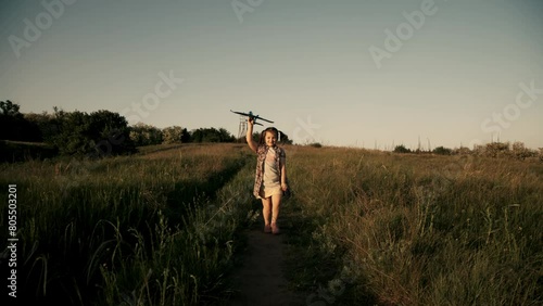 A happy girl runs with a toy plane across a field in the rays of the sun. Children play with a toy airplane in the countryside. The girl dreams of flying and becoming a pilot. photo