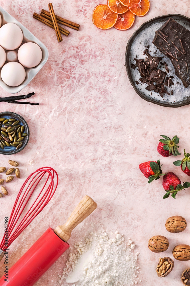 Close up of making a pink counter with various baking ingredients such as flour, eggs, chocolate, strawberries, nuts and rolling pin.