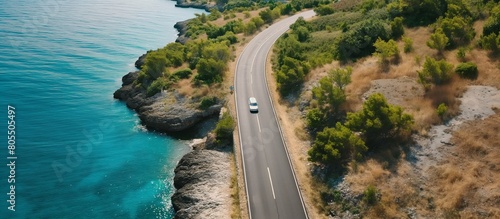 Mountain road near blue sea in summer. Top view of road, trees, azure water, mountain. Beautiful landscape with highway, rocks, sea coast. Mountain road by the sea, aerial view. Travel concept.