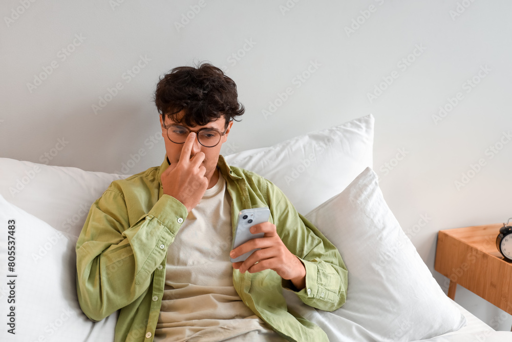 Young man with eyeglasses using mobile phone in bedroom