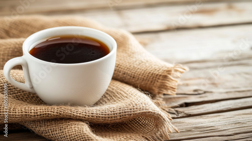 A cup of coffee is sitting on a wooden table with a blanket underneath it